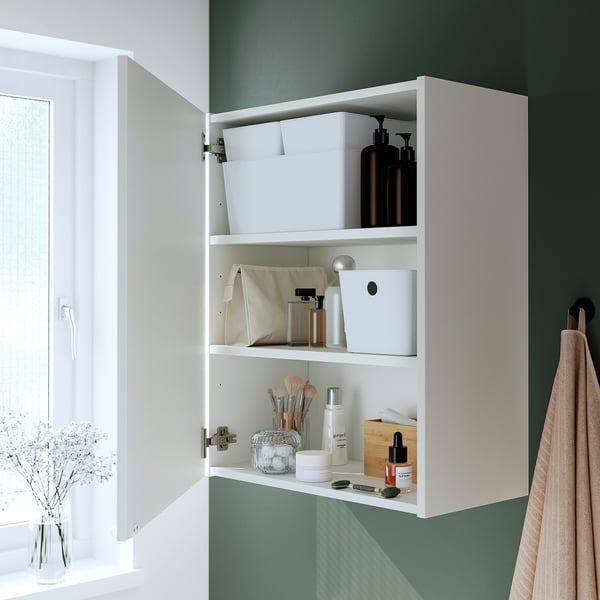 Bílá skříňka s otevřenými dveřmi, vystavená na toaletních věcech jako lahve a sklenice na policích. Integrované klapky pro měkké zavírání.