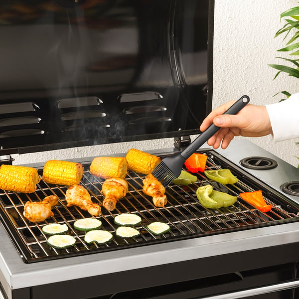 Osoba grilující jídlo štětcem, nanášející omáčku. Kukuřice, kuře a zelenina na grilu.
