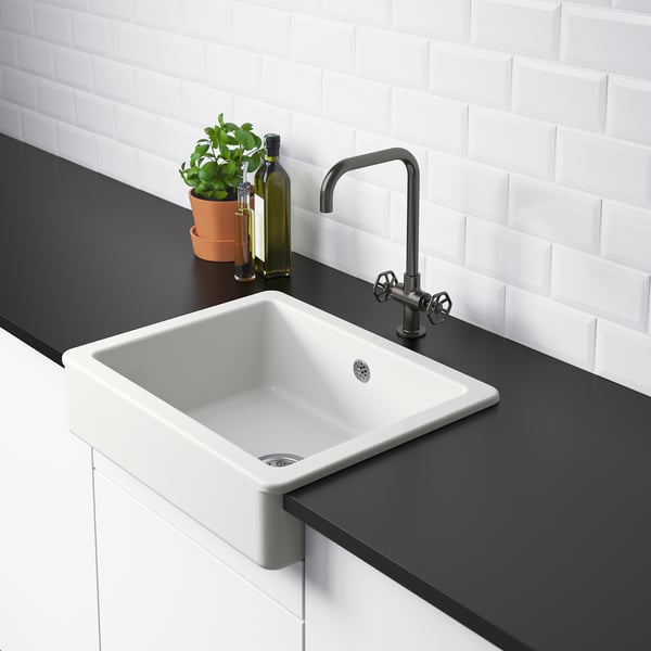 Bílý farmářský dřez se stříbrnou baterií, černou pracovní deskou, zelenou rostlinou a lahví na olivový olej.