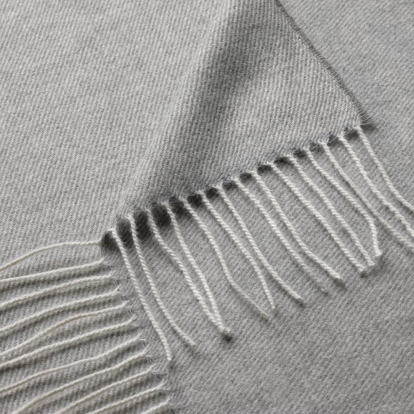 Měkká, šedá přikrývka se složitými, rovnoměrně rozmístěnými třásněmi podél okraje.