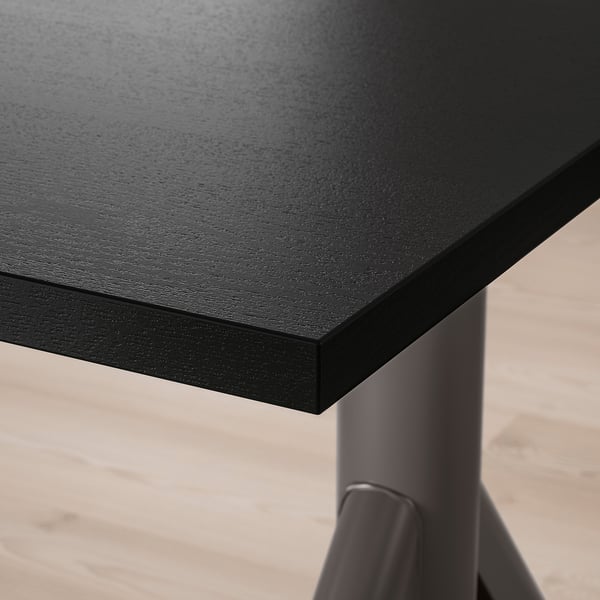 Detailní záběr na moderní černý stůl s hladkým, odolným povrchem a robustními kovovými nohami, který představuje vysoce kvalitní materiály a design.