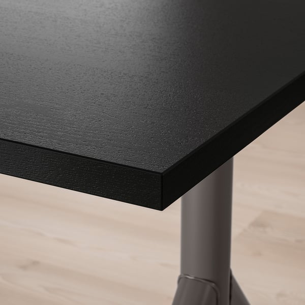 Detailní záběr na elegantní černou desku stolu s hladkým, rovným povrchem, podepřenou robustními kovovými nohami.