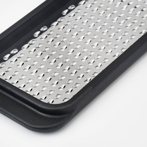 Detailní záběr struhadla z nerezové oceli v černém plastovém rámu, který ukazuje ostré, rovnoměrně rozmístěné otvory a odolný design.