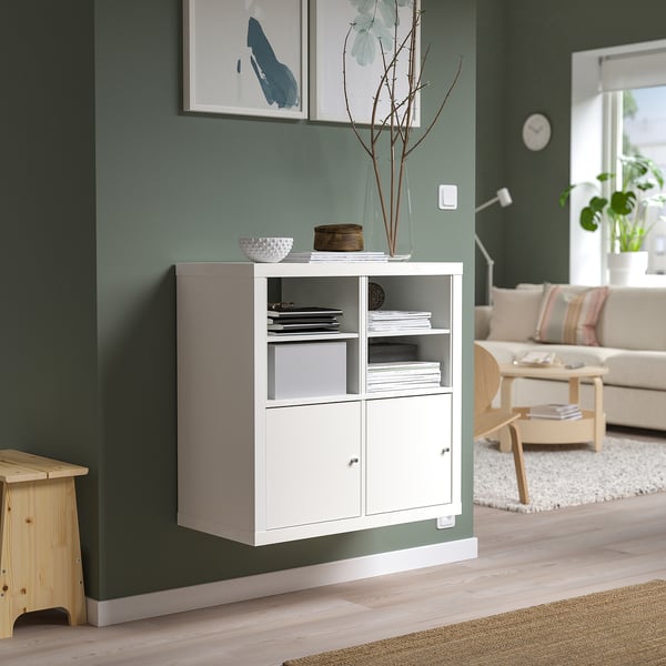 KALLAX police s knihami a dekoracemi proti zelené stěně, pohovce a lampě.