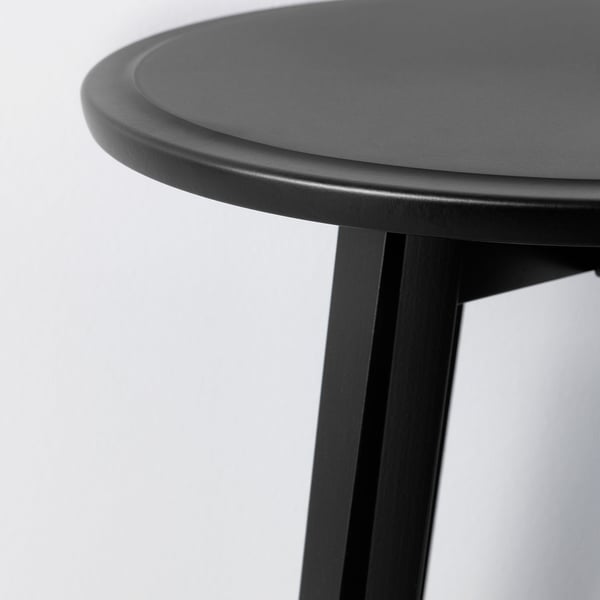 Detail moderního černého stolu s hladkými, zaoblenými hranami a robustními nohami. Vykazuje vysoce kvalitní design a povrchovou úpravu.