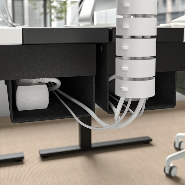Psací stůl se zabudovaným systémem vedení kabelů. Kabely zastrčené uvnitř přihrádky, což zlepšuje organizaci pracovního prostoru.