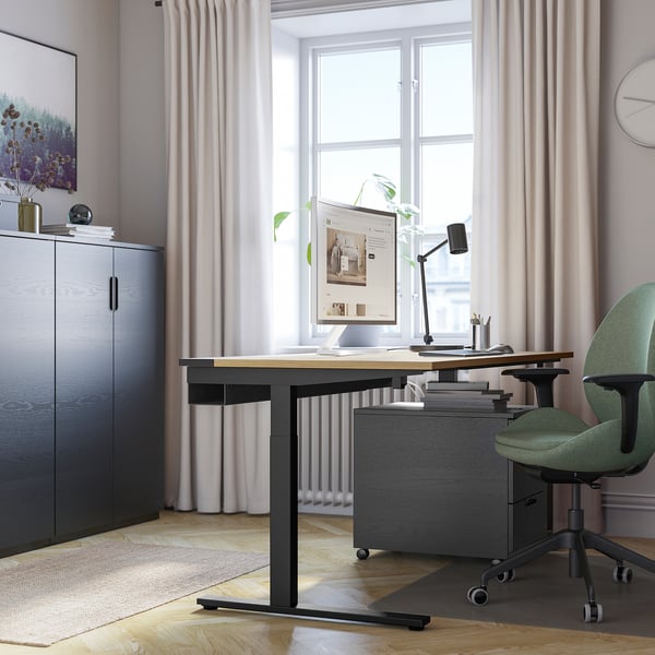 Moderní pracovní prostor s psacím stolem MITTZON, zelenou židlí, velkým úložným prostorem. Minimalistický design, dobře osvětlený.