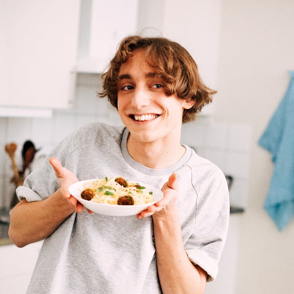 Osoba držící misku se špagetami a masovými kuličkami ve stylové misce z tvrzeného skla vhodné do mikrovlnné trouby.