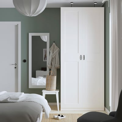 Moderní ložnice s velkou bílou šatní skříní PAX, vysokým zrcadlem a šalvějově zelenými stěnami.