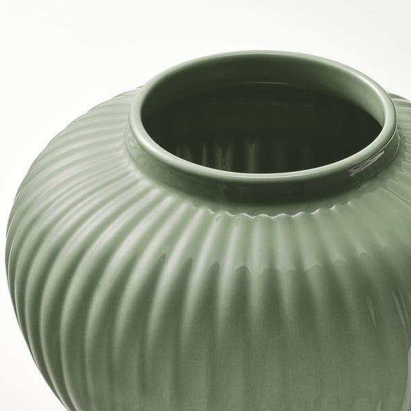 Zelená glazovaná kameninová váza, s drážkovaným designem a hladkým povrchem, stojící na bílém pozadí.