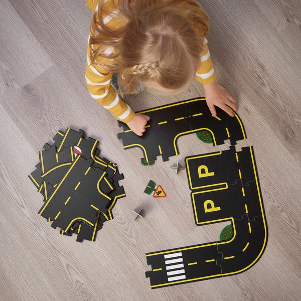 Holčička si hraje s puzzle RÄVUNGE na podlaze, sestavuje dílky silnice a dopravní značky, zlepšuje řešení problémů a kreativitu.