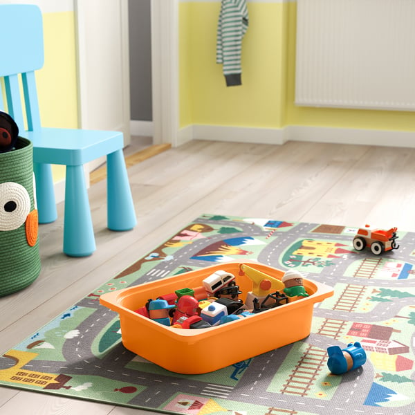 Barevná krabice na hračky na koberci s auty a figurkami. Modrá židle a žlutě natřená stěna v pozadí.