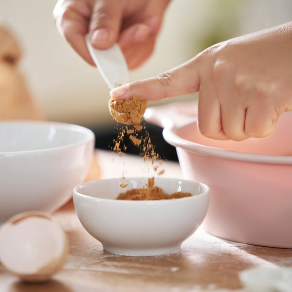 Člověk prosévá koření do misky pomocí odměrky pro přesné měření.
