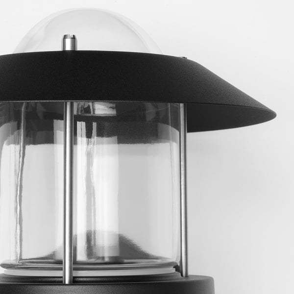 Černá nástěnná lampa se stínidlem z čirého skla, s odolnou kovovou konstrukcí, vhodná pro venkovní použití.