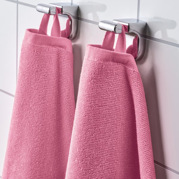 Na nástěnných háčcích jsou úhledně zavěšeny dva růžové froté ručníky, které předvádějí svou savou, měkkou strukturu a rychleschnoucí žebrovou vazbu.