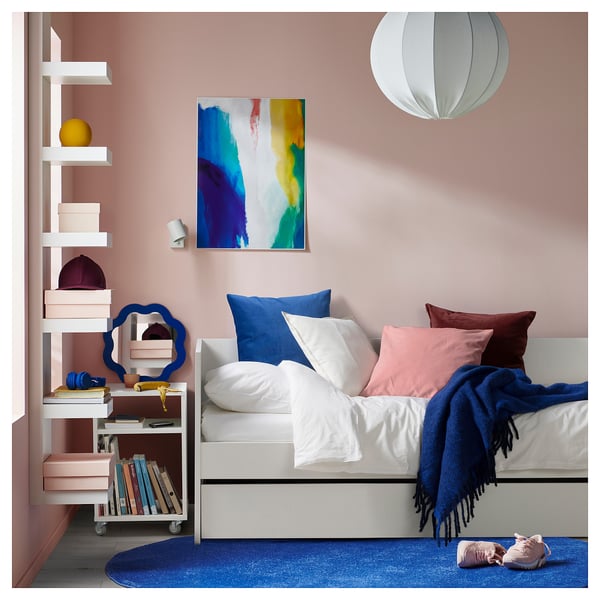 Útulná ložnice s moderní bílou pohovkou s modrými a růžovými akcenty, barevným kobercem a stylovým dekorem.