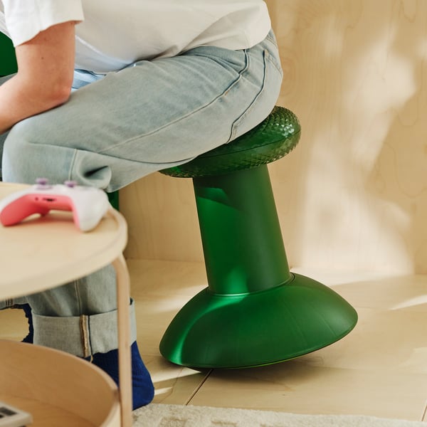 Osoba na zelené YXSTABY stoličce IKEA s ovladačem Xbox na blízké dřevěné stoličce.