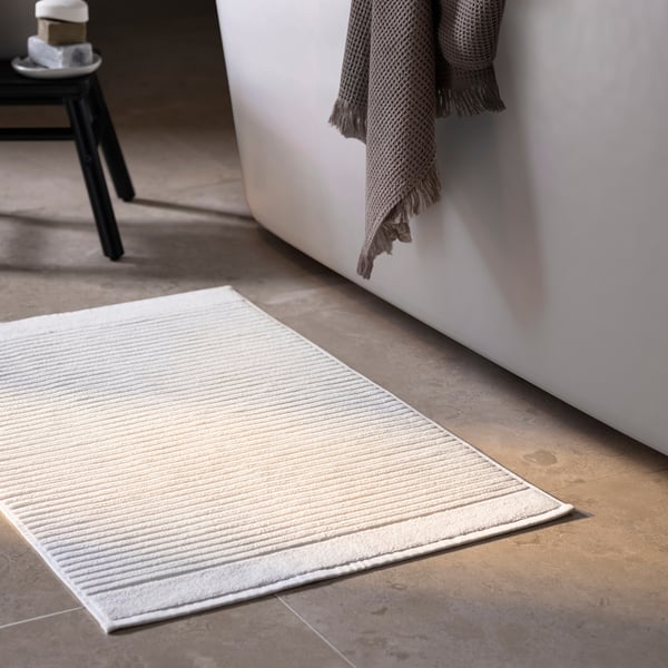 Bathroom with white terry cloth mat, grey towel, black stool.