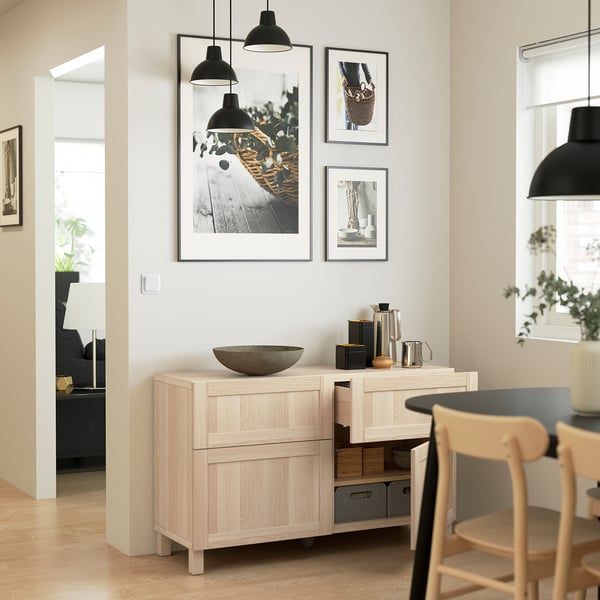 Minimalist dining area with wood storage, adjustable shelves, and coffee setup under art and lights.