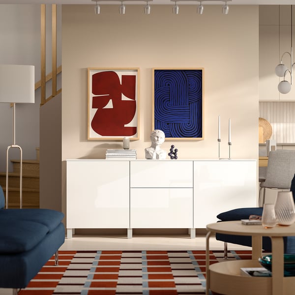 Modern living room, white BESTÅ sideboard, colourful art, blue chair, wooden table, track lighting.