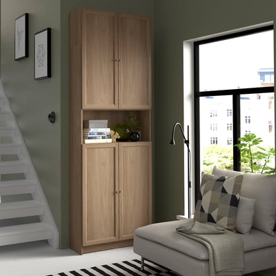 Modern room with tall wooden BILLY bookcase, grey couch, and large window.