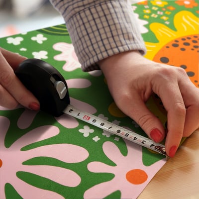 Person measures fabric with tape, using mouse on colourful, patterned material.