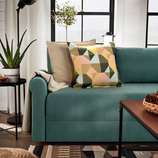 Modern living room with teal sofa, colourful pillows, plants, and wooden table.
