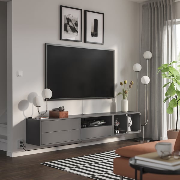 Modern living room with tv on EKET unit, blonde floors, black/white rug, tall lamps.