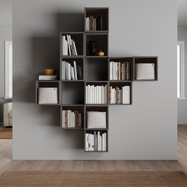 Modern wall-mounted grey bookshelf, filled with books & decorative items. Asymmetrical design with multiple compartments.
