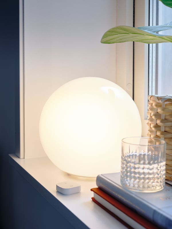 A FADO table lamp, white with round glass shade, remote on shelf. Modern, soft mood lighting.