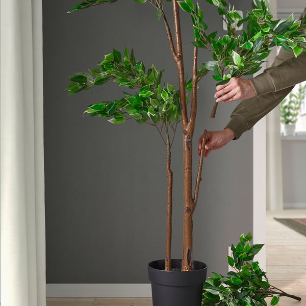 Person arranges lifelike artificial leaves on potted plant indoors.