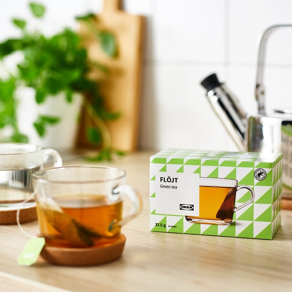 Box of green tea bags on table near tea cup.