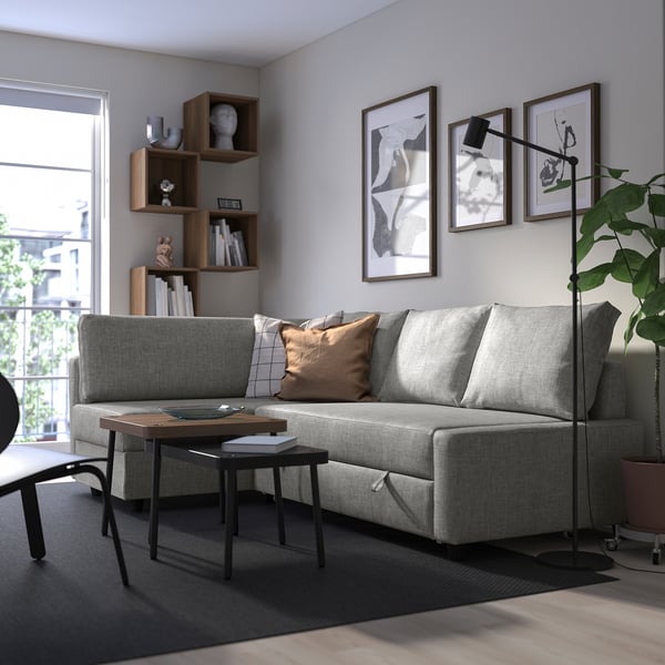 Modern living room with grey FRIHETEN sofa-bed, chaise, cushions. Decorated shelf and large window behind.