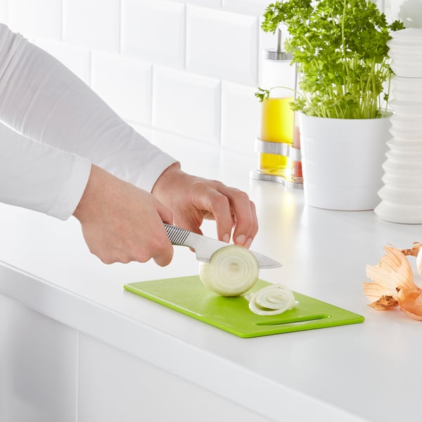 Person slices onion on green cutting board, with knife, on countertop.