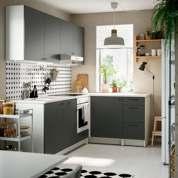 L-shaped grey kitchen: dark cabinets, marble counter, light, plant, open shelves, wood stool.