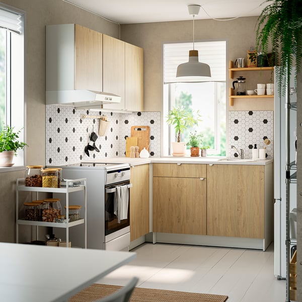 Contemporary l-kitchen: light wood cabinets, marble counters, black backsplash, tall stove, metal cart, pendants, large windows, natural light.