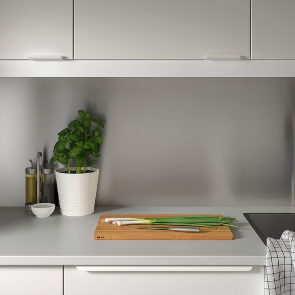Minimalist grey kitchen counter. Small potted plant, oil bottles, knife, scallions, and cutting board with LYSEKIL wall panel.