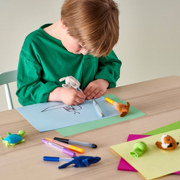 A child is drawing on a large piece of paper with markers and scissors on the table.