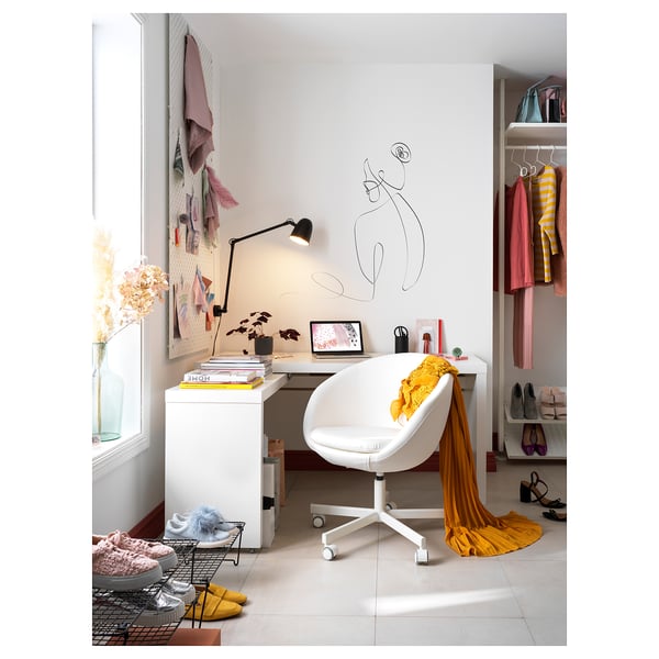 Minimalist home office with white desk, chair, and closet. Decor includes wall art, lamp, and clothes rack.