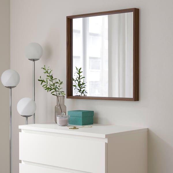 NISSEDAL mirror over white chest, reflecting window, with lamp, vase, and turquoise box.