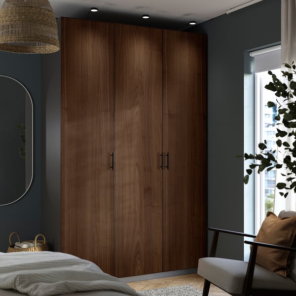 Modern bedroom with dark wood PAX wardrobe, grey chair, and city view.
