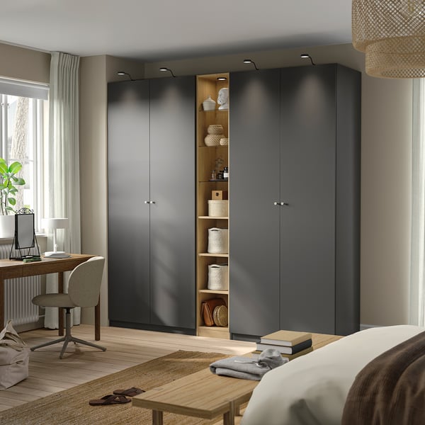 Modern bedroom with large grey PAX wardrobe and open shelves, featuring desk and chair, with natural light from a window with white curtains.