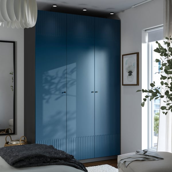 Modern bedroom with tall blue PAX closet, large windows, cosy seating, and decor.