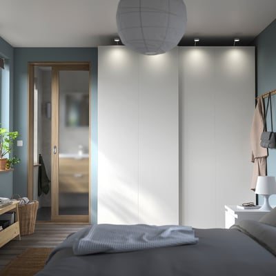 Modern bedroom with grey bed, white wardrobe, wooden door, pendant light, and bedside table with lamp.