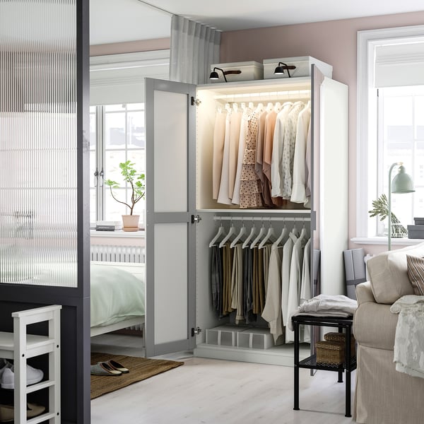 Modern, open wardrobe displaying clothes, with integrated lighting, adjustable feet, and organised interior.