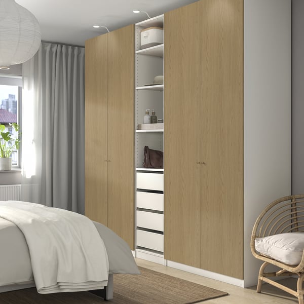 Modern bedroom with PAX wardrobe, open storage, wicker chair by window.