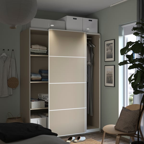 Modern bedroom with beige PAX wardrobe, featuring shelves, clothes, and decorations.