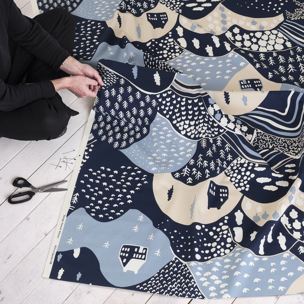 Person arranges patterned fabric with mountain designs. Scissors, pins nearby. Ideal for sewing projects.