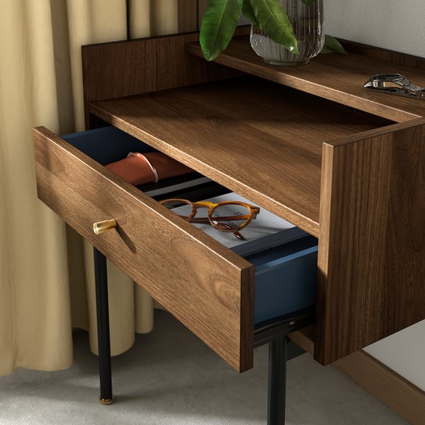A wooden bedside table named RÅDMANSÖ in walnut tone, featuring a drawer and an open shelf. The drawer has a blue interior and brass-like handles.