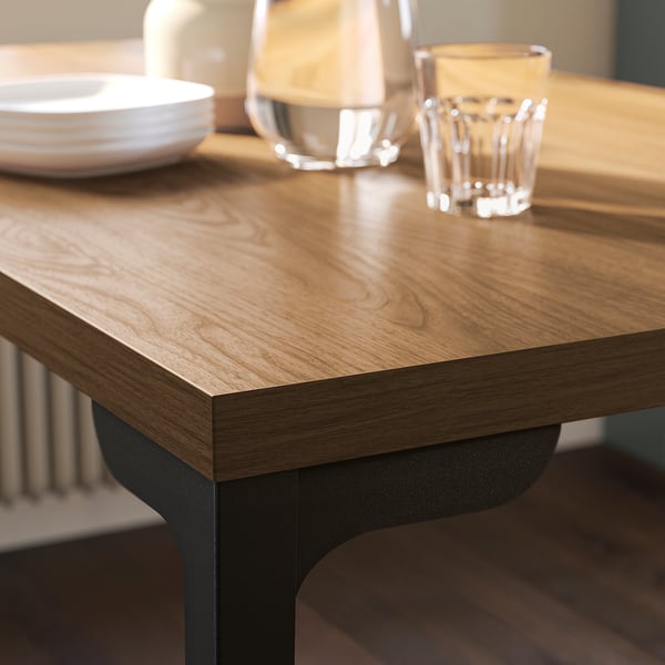 Wooden table with dark metal legs, set with simple white dishware and clear glassware, reflecting a clean and modern dining setup.